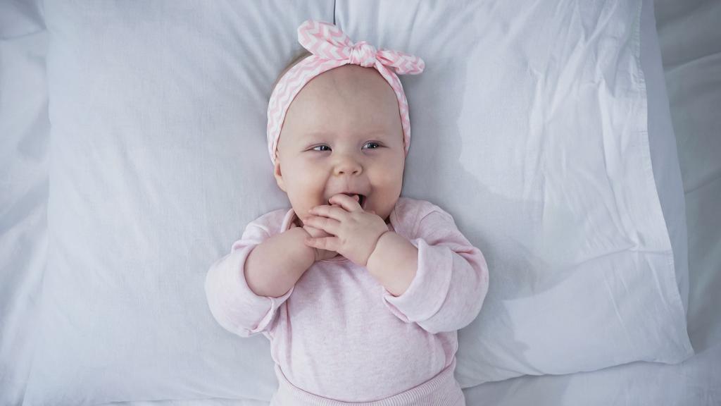vue du haut de bébé fille dans le bandeau avec arc sucer les doigts tout en étant couché sur le lit - Photo, image