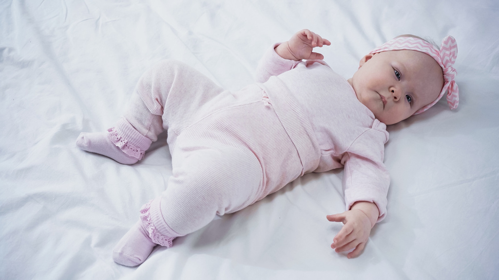 high angle view of baby girl in headband with bow lying on bed - Photo, Image