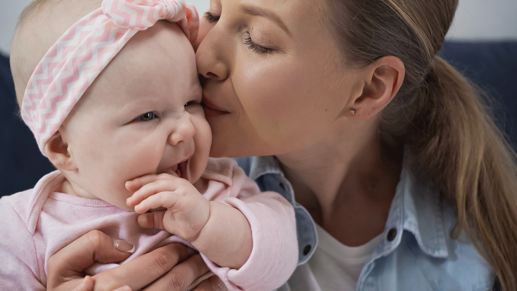 huolehtiva äiti suutelee vauvan tyttären poskea  - Valokuva, kuva