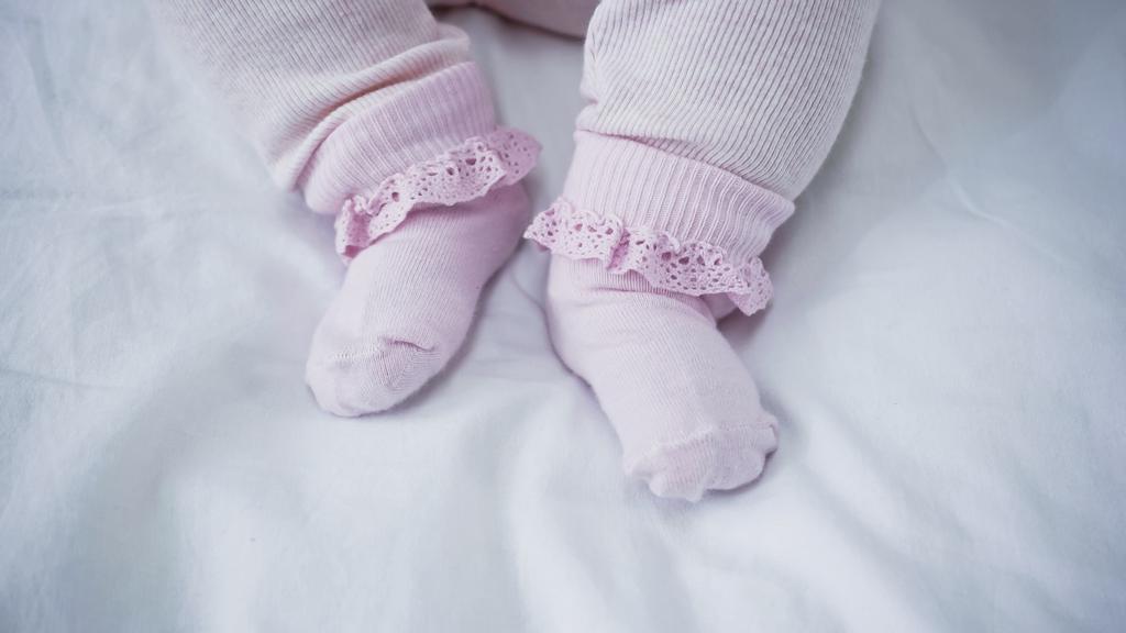 καλλιεργημένη άποψη του μωρού σε romper και κάλτσες στο κρεβάτι - Φωτογραφία, εικόνα