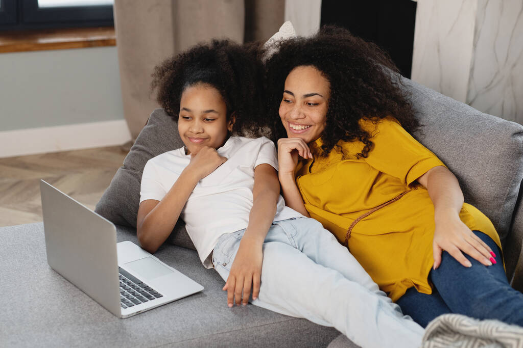 アフリカ系アメリカ人の母親と彼女の娘を使用してノートパソコンソファに横たわって. - 写真・画像