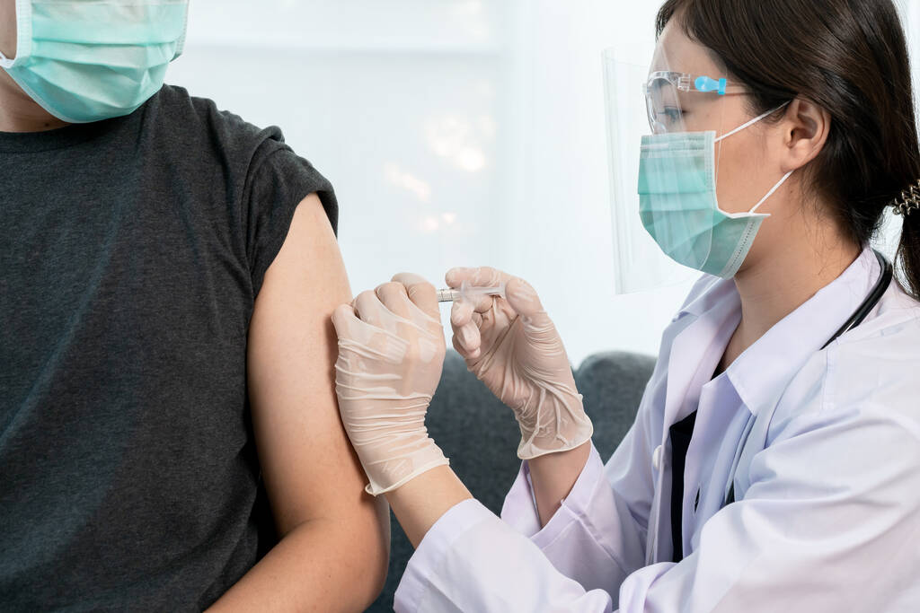 Asiatischer Facharzt injiziert Coronavirus 2019-nCoV oder COVID-19 Impfstoff am Arm des männlichen Patienten aus nächster Nähe, COVID19 Impfung über Schutz und Aufbau von Antikörpern - Immunität gegen Coronavirus. - Foto, Bild