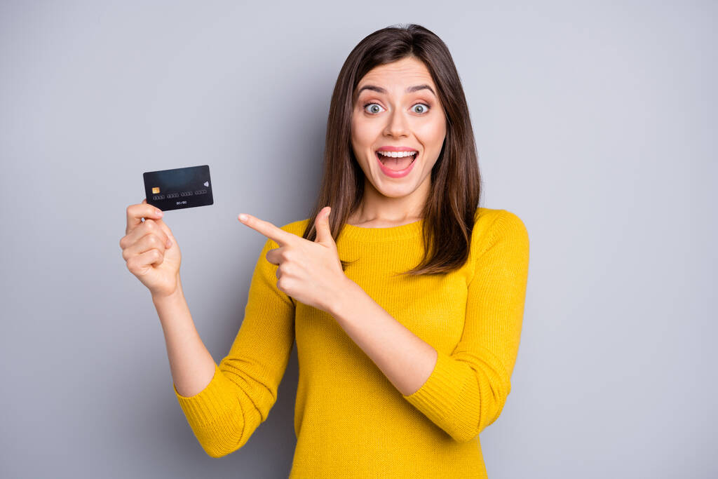 Retrato de chica alegre bastante sorprendido sosteniendo en las manos demostrando novedad tarjeta bancaria aislado sobre fondo de color gris - Foto, imagen