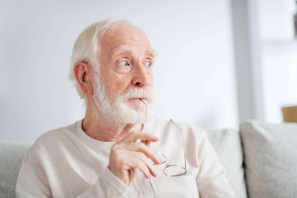 Фото пожилого человека пенсионера сидеть диван-хаус в помещении серьезно мыслящие мечты мечтательный взгляд пустое пространство - Фото, изображение