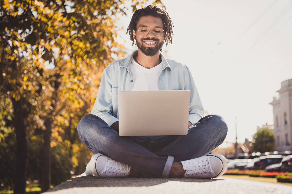 Full size photo of attractive cheerful young afro american man sit city center look laptop wear in outdoors outside - Photo, Image