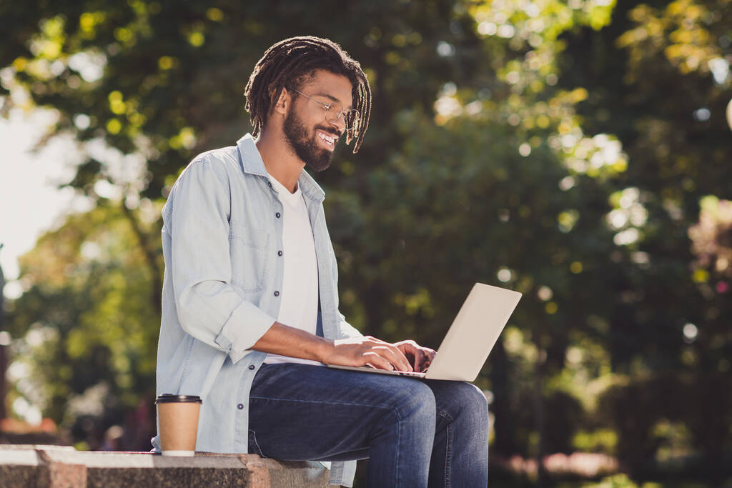 Profil strona zdjęcie uroczy młody wilgotny skóra człowiek siedzieć praca laptop nosić okulary na zewnątrz w parku na zewnątrz - Zdjęcie, obraz