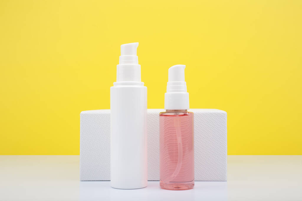 Gesichtscreme in weißer Röhre und rosa Reinigungsschaum in transparenter Röhre vor gelbem Hintergrund mit Kopierraum. - Foto, Bild