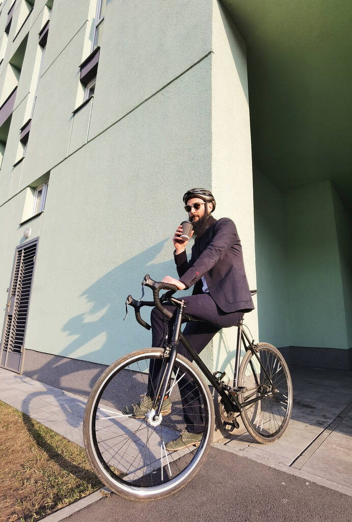 Beginnen Sie den neuen Tag mit frischem Kaffee. Millennial-Geschäftsmann hält eine Tasse Kaffee in der Hand, lehnt an seinem Fahrrad und blickt auf den freien Raum. - Foto, Bild