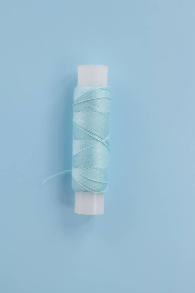 Sewing production concept. Repair of clothes, sewing a new collection for the season. Spool of white thread on a blue background close-up. Minimal top view. - Photo, Image