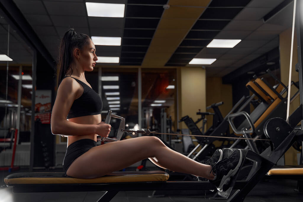 筋肉フィットネスジムでケーブルを使用してマシンに戻るための重い運動をする女性アスリート - 写真・画像