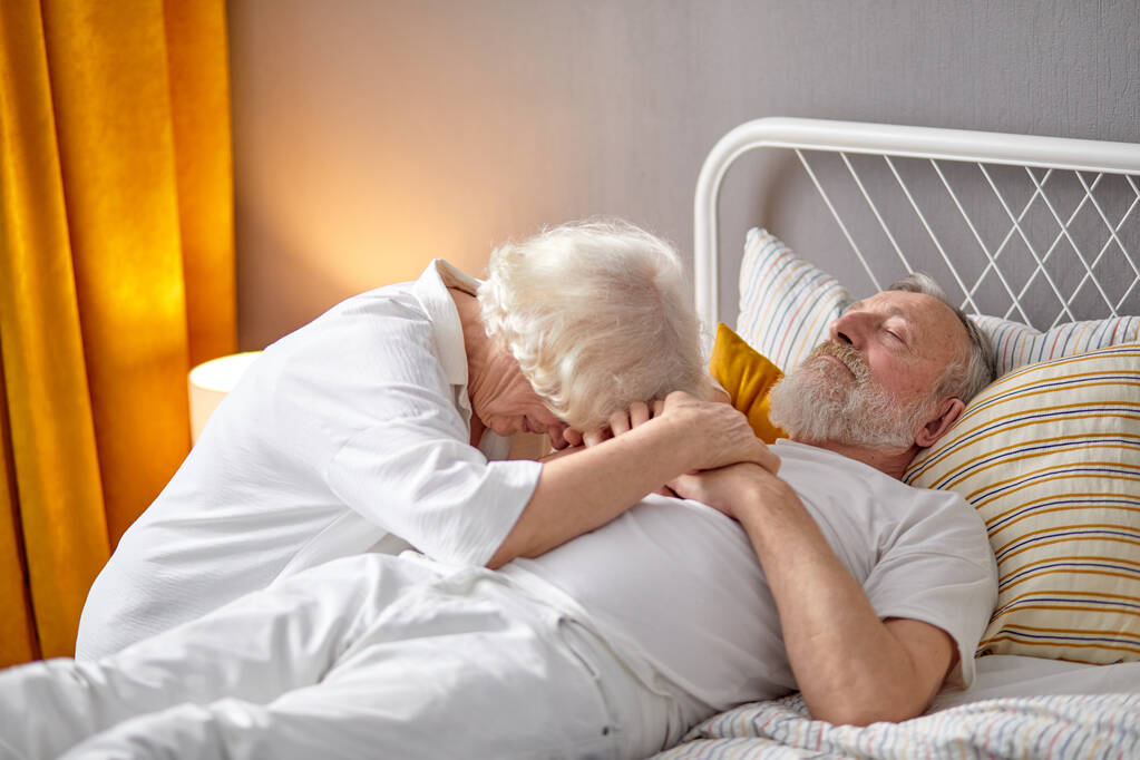 Vanhempi nainen istuu kuolevan aviomiehen vieressä makaamassa sängyssä ja itkemässä - Valokuva, kuva