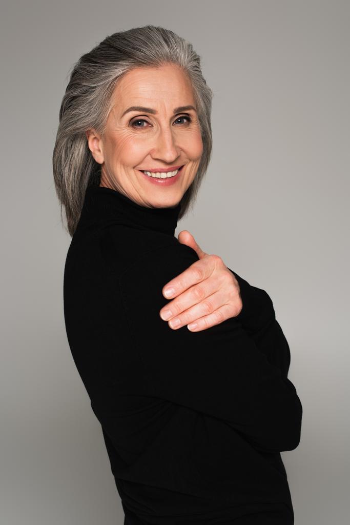 Портрет женщины в черном свитере, улыбающейся изолированно на сером  - Фото, изображение