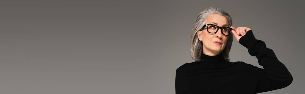 Mujer sosteniendo anteojos y mirando hacia otro lado aislado en gris, estandarte  - Foto, Imagen