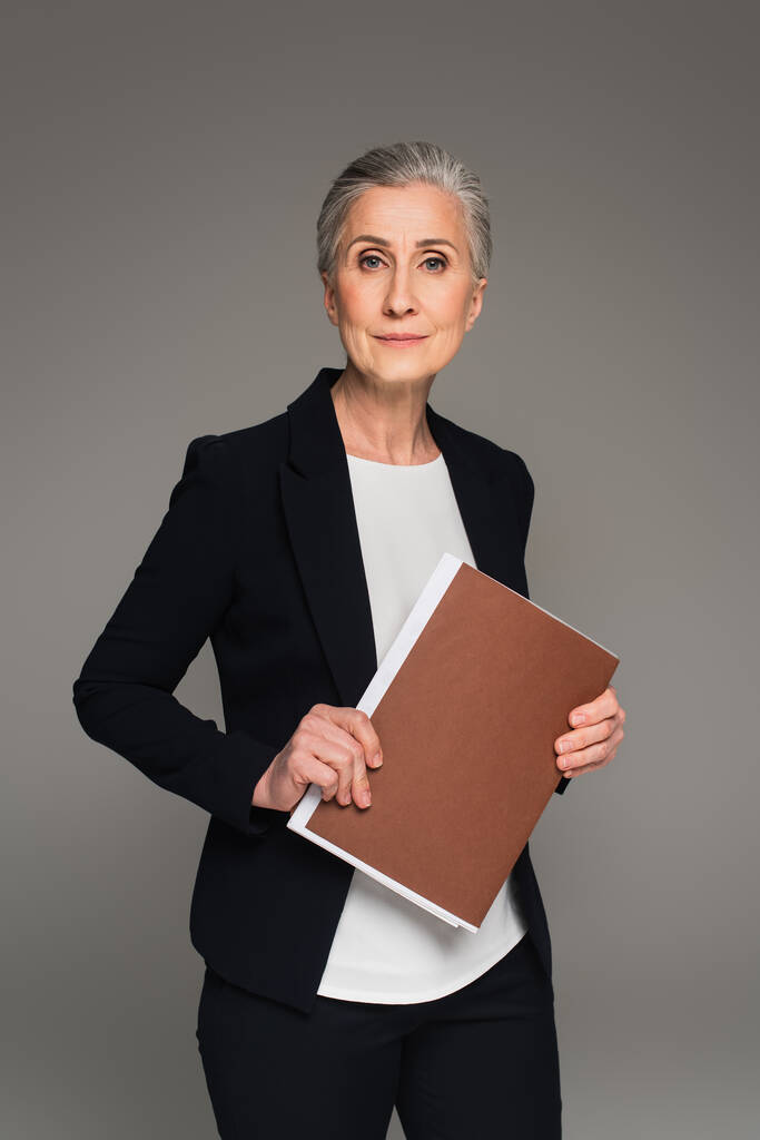 Imprenditrice in abbigliamento formale che tiene la cartella di carta isolata su grigio  - Foto, immagini