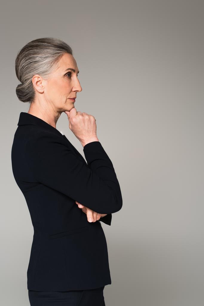 Vue latérale de coûteuse femme d'affaires mature regardant loin isolé sur gris  - Photo, image