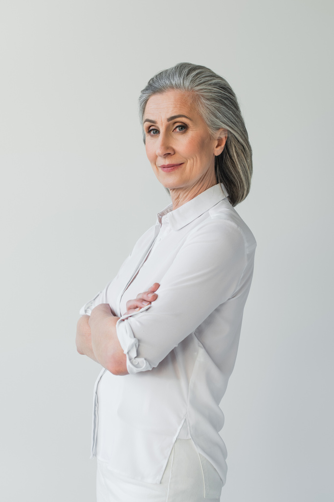 Grey haired woman in white clothes looking at camera isolated on grey  - Photo, Image