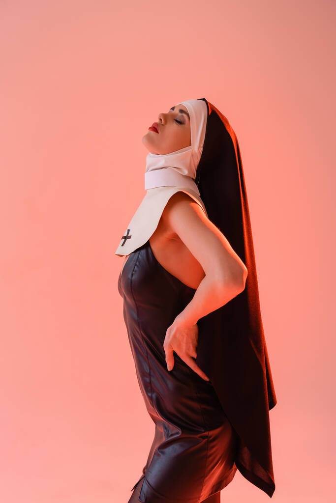 若いです修道女で革のドレス姿ピンクに隔離された目でポーズ - 写真・画像