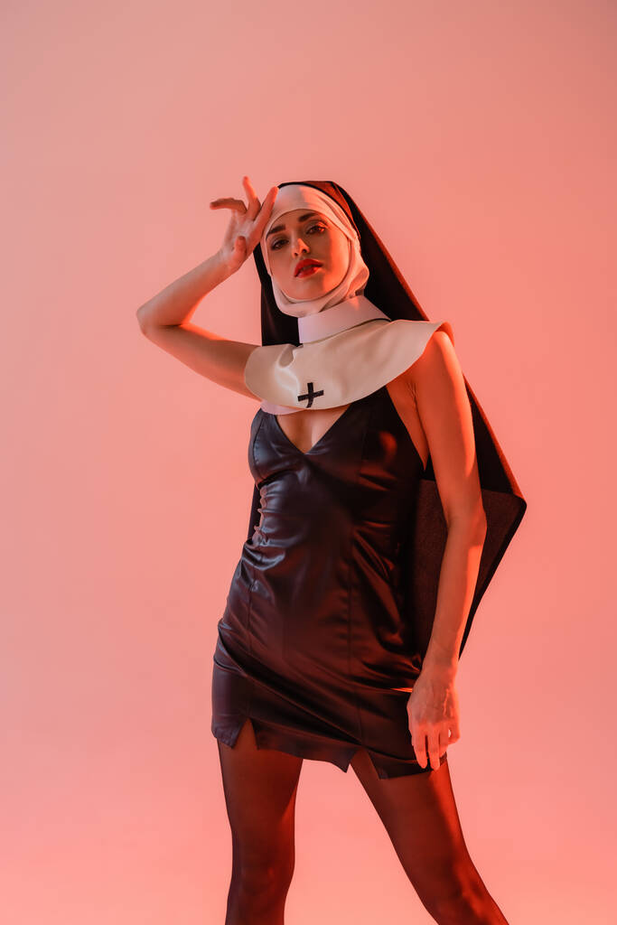 sensual nun looking at camera while holding hand near head isolated on pink - Photo, Image