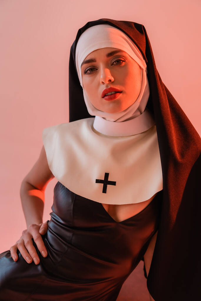 sensual nun in sexy dress looking at camera isolated on pink - Photo, Image