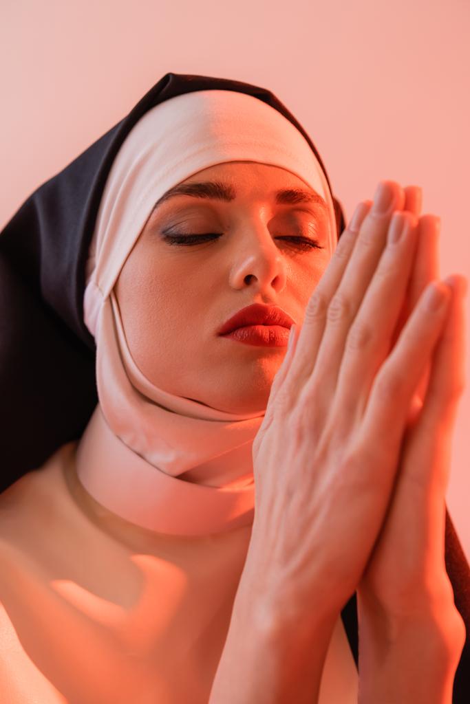 молода черниця молиться із закритими очима ізольовано на рожевому
 - Фото, зображення