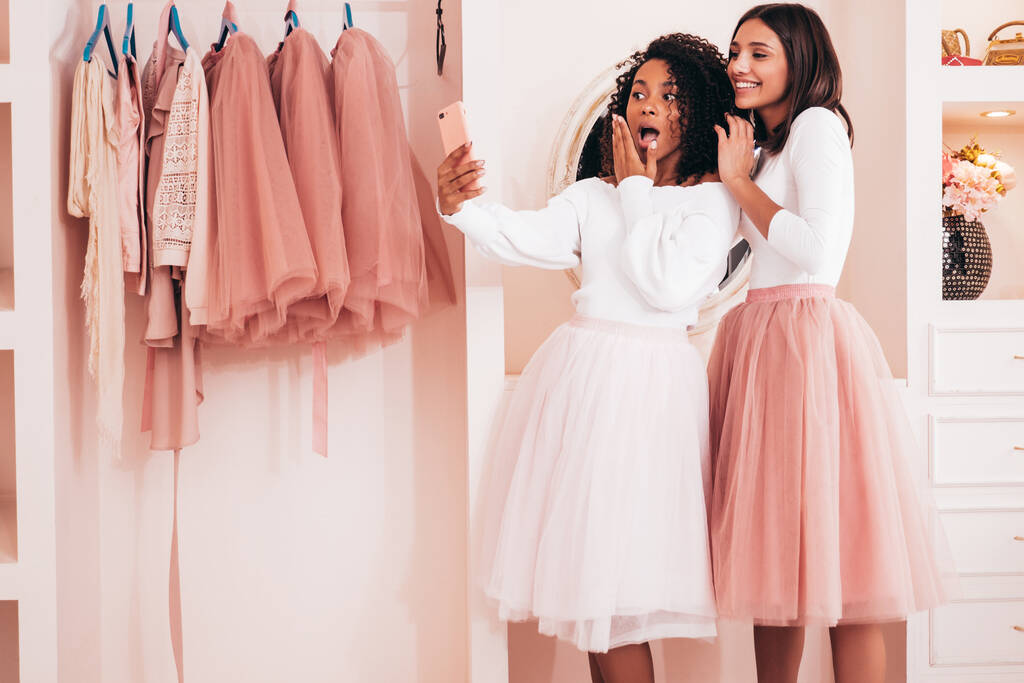 Zwei junge, schön lächelnde internationale Hipsterinnen in trendigen Sommerkleidern. Sexy unbeschwerte Frauen posieren in pinkfarbenen Kleiderschränken. Positive Modelle, die Spaß haben. Konzept der Freundschaft: Selfie machen - Foto, Bild