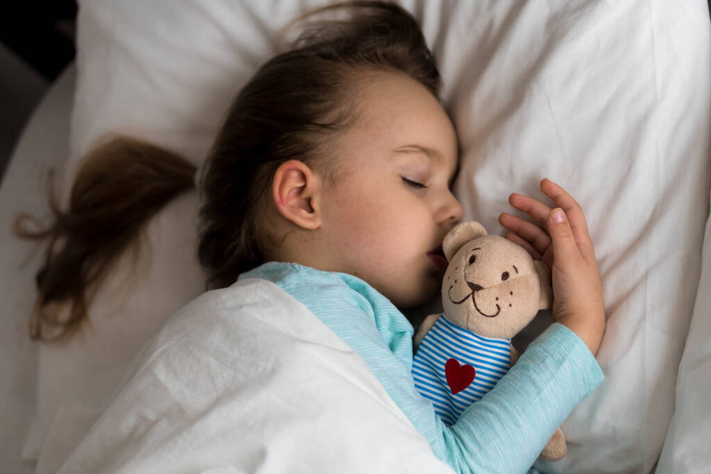 Authentisches Porträt kranker süßer kaukasischer kleiner Vorschuljunge im blauen Schlaf mit Teddybär auf weißem Bett. Mittags ruhen die Kinder. Pflege, Medizin und Gesundheit, Kindheit, Elternschaft, Lebenskonzept - Foto, Bild