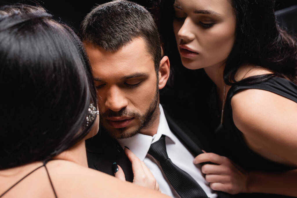 сексуальные брюнетки, соблазняющие молодого бизнесмена, изолированного от черного - Фото, изображение