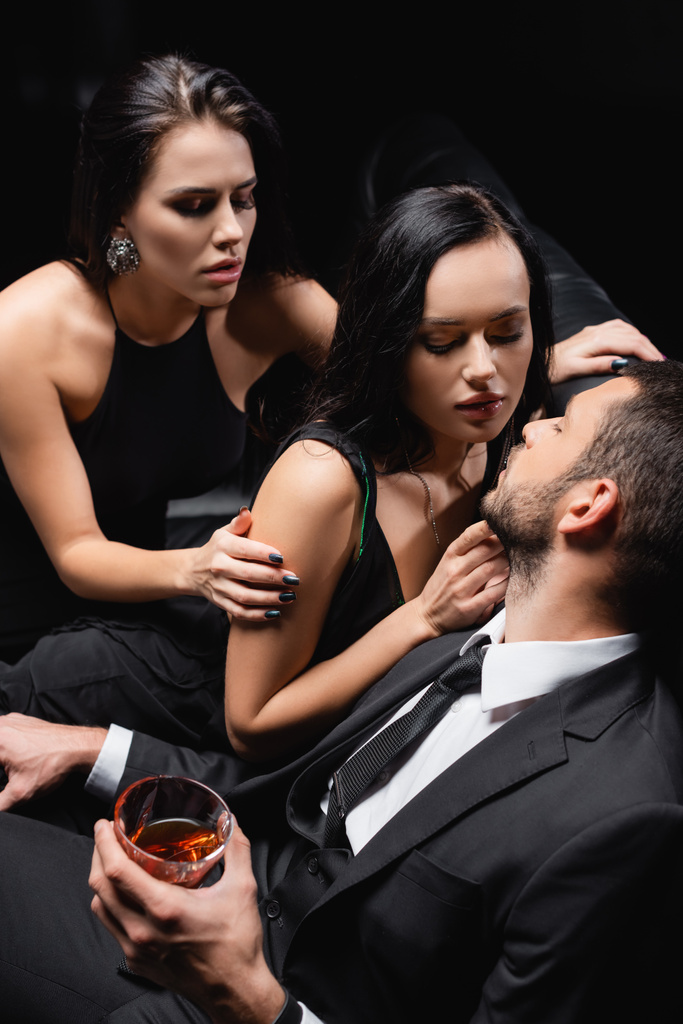 Mann hält Glas Whiskey in der Nähe sexy Frauen verführt ihn isoliert auf schwarz - Foto, Bild