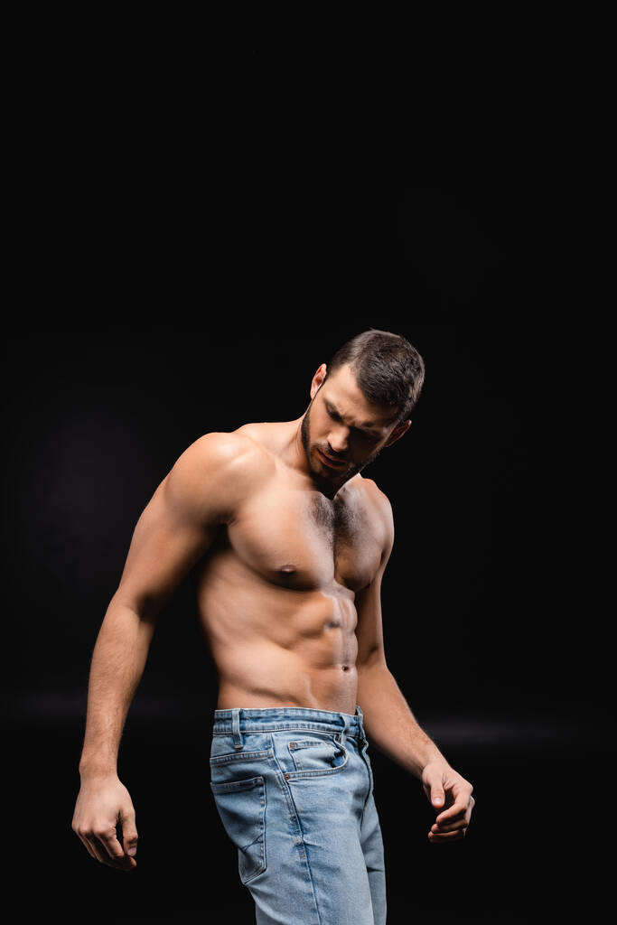 без рубашки, мускулистый мужчина в джинсах позирует на черном фоне - Фото, изображение