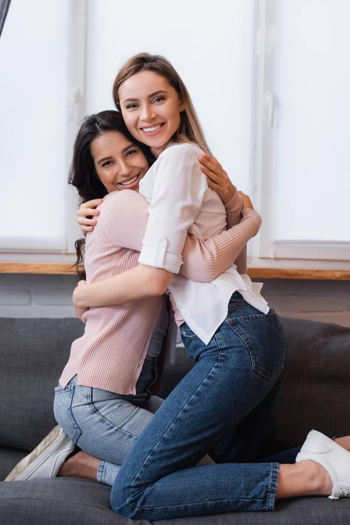 Positives lesbisches Paar beim Umarmen im modernen Wohnzimmer - Foto, Bild
