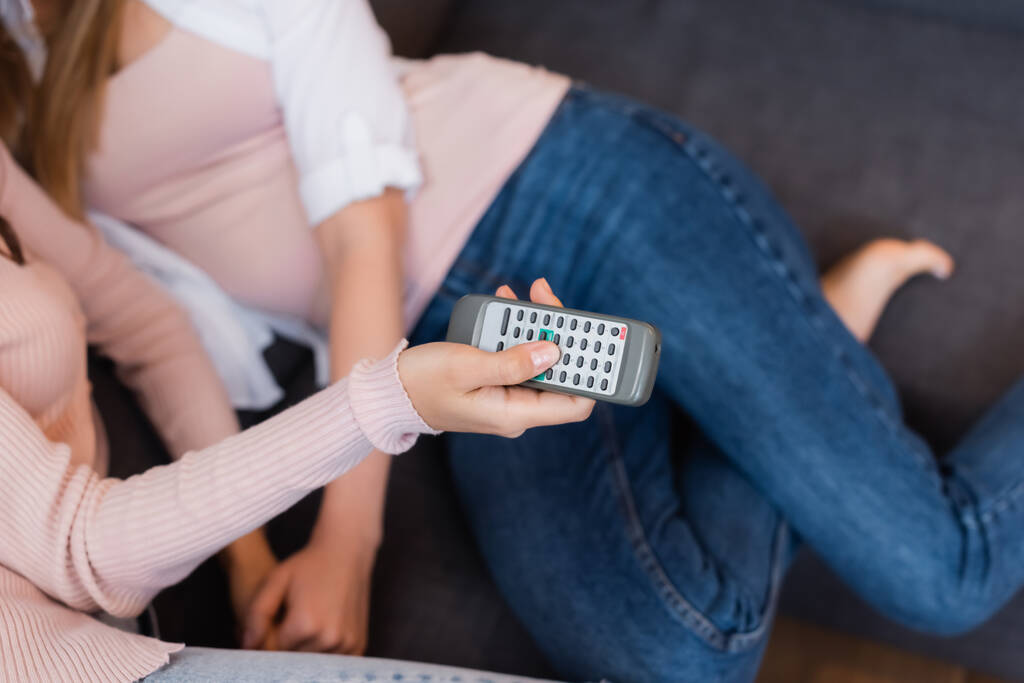 cropped view of woman holding remote controller while chilling with girlfriend in living room - Foto, Imagem