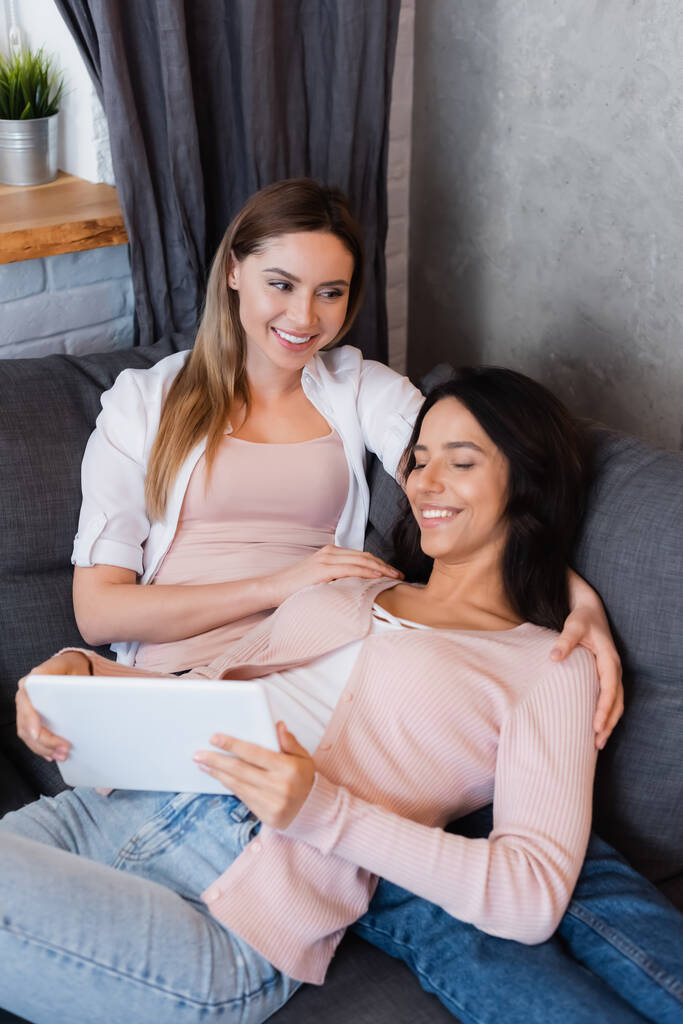 smiling lesbian couple watching movie on digital tablet at home  - Photo, image