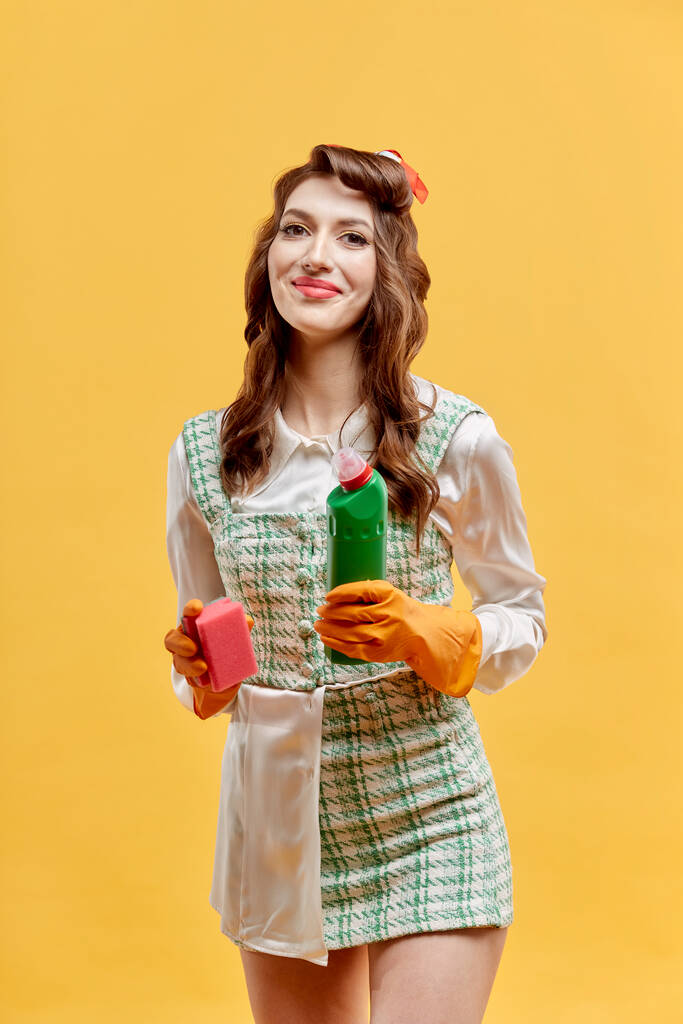 Una mujer limpiadora en un vestido corto sostiene herramientas para limpiar la casa. - Foto, Imagen