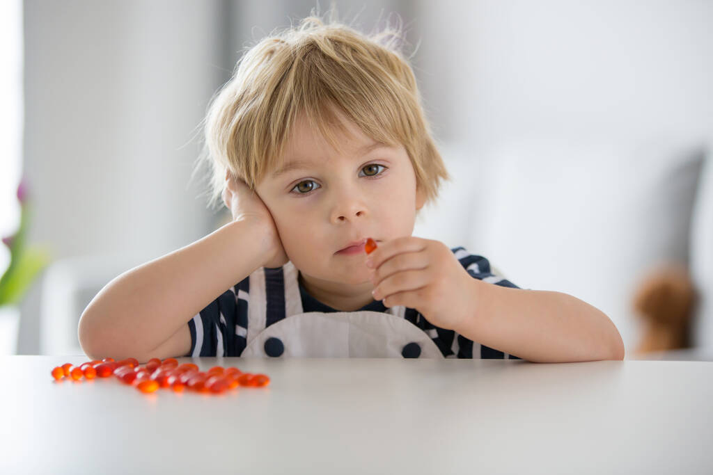 Lindo niño pequeño, niño pequeño, comer alfa omega 3 suplemento infantil píldoras vitamínicas en casa para una mejor imunidad - Foto, Imagen