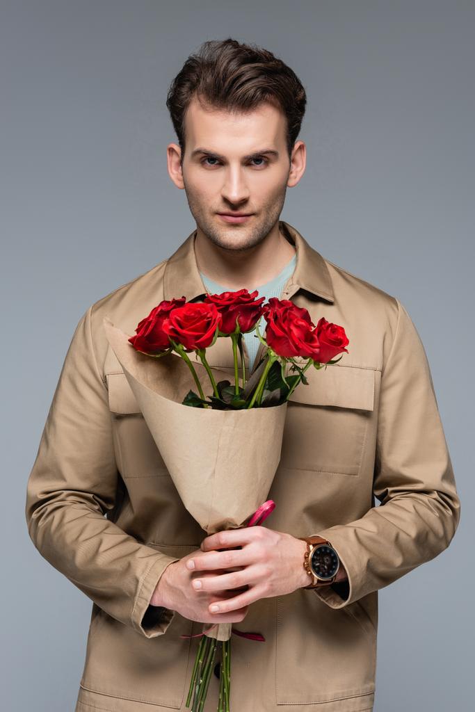 elegante uomo che tiene bouquet di rose rosse isolate su grigio - Foto, immagini