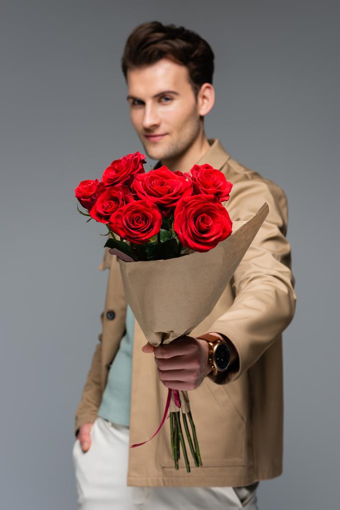 homályos trendi férfi kezében csokor vörös rózsa csomagolva papír elszigetelt szürke - Fotó, kép
