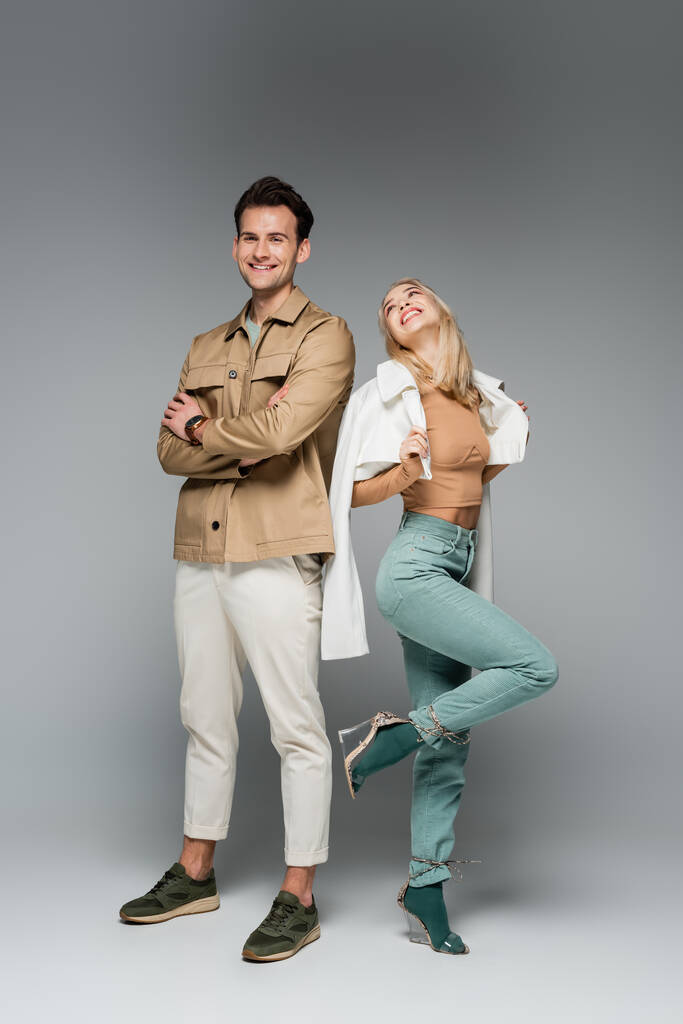 comprimento total de modelos na moda em calças e jaquetas posando e sorrindo no cinza - Foto, Imagem