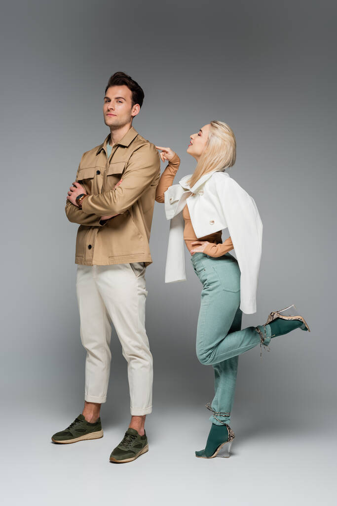 longueur totale du modèle élégant en pantalon et veste pointant vers l'homme posant sur le gris - Photo, image