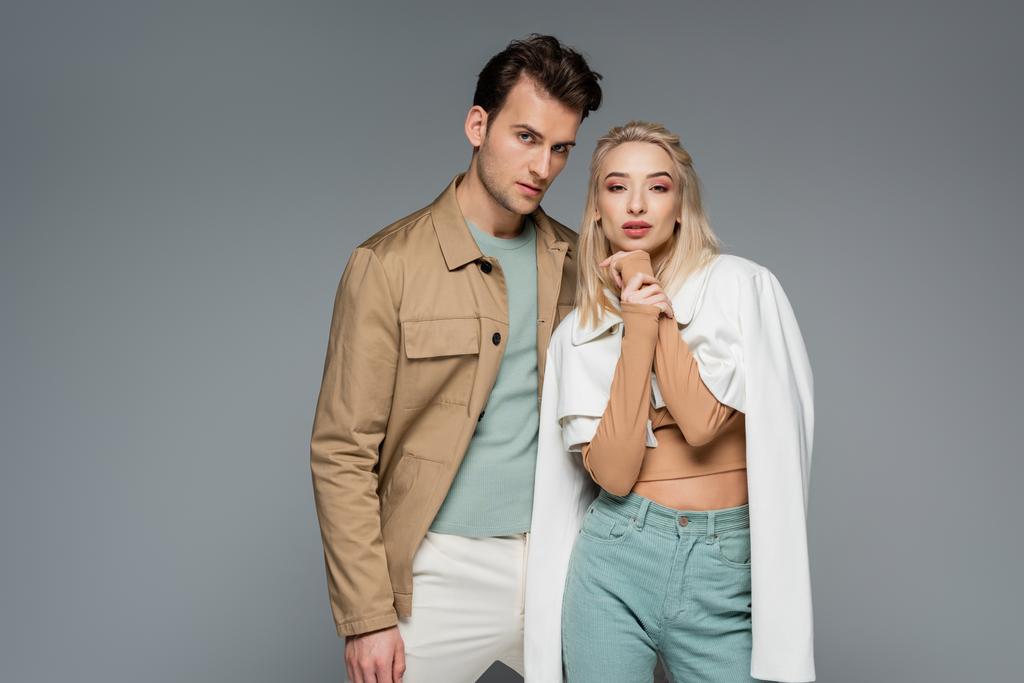 stijlvolle modellen in broeken en jassen poseren geïsoleerd op grijs - Foto, afbeelding