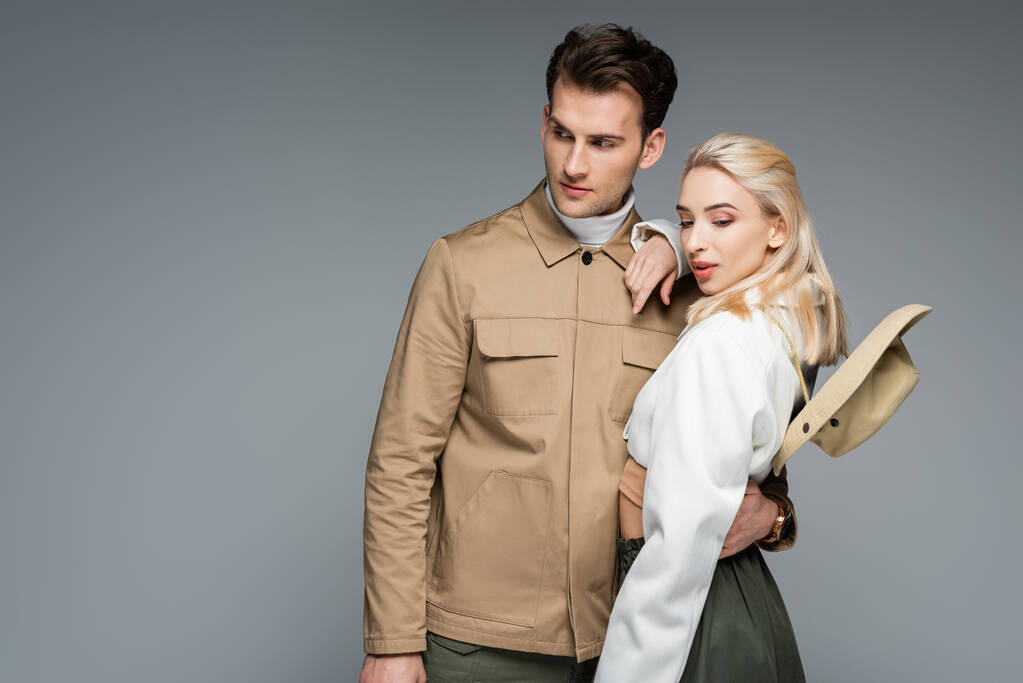 stijlvolle man in jas knuffelen blonde vrouw geïsoleerd op grijs - Foto, afbeelding