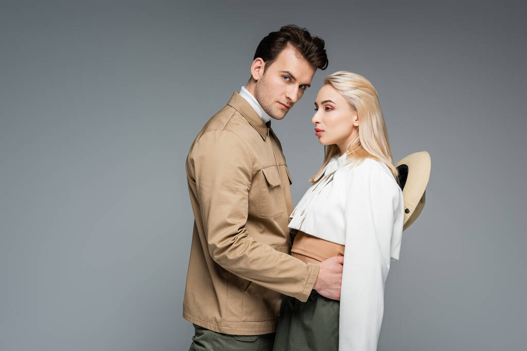 stylish man in jacket hugging blonde young woman isolated on grey - Photo, Image