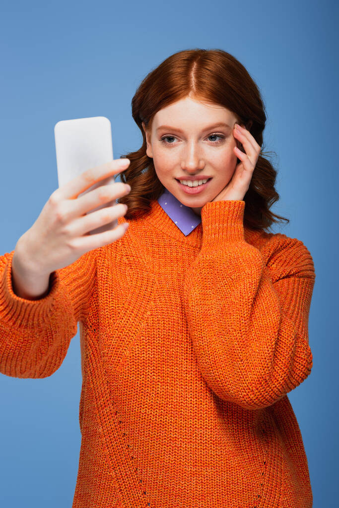 幸せな赤毛女性でオレンジセーター取ります自画撮り上のスマートフォン絶縁オン青 - 写真・画像