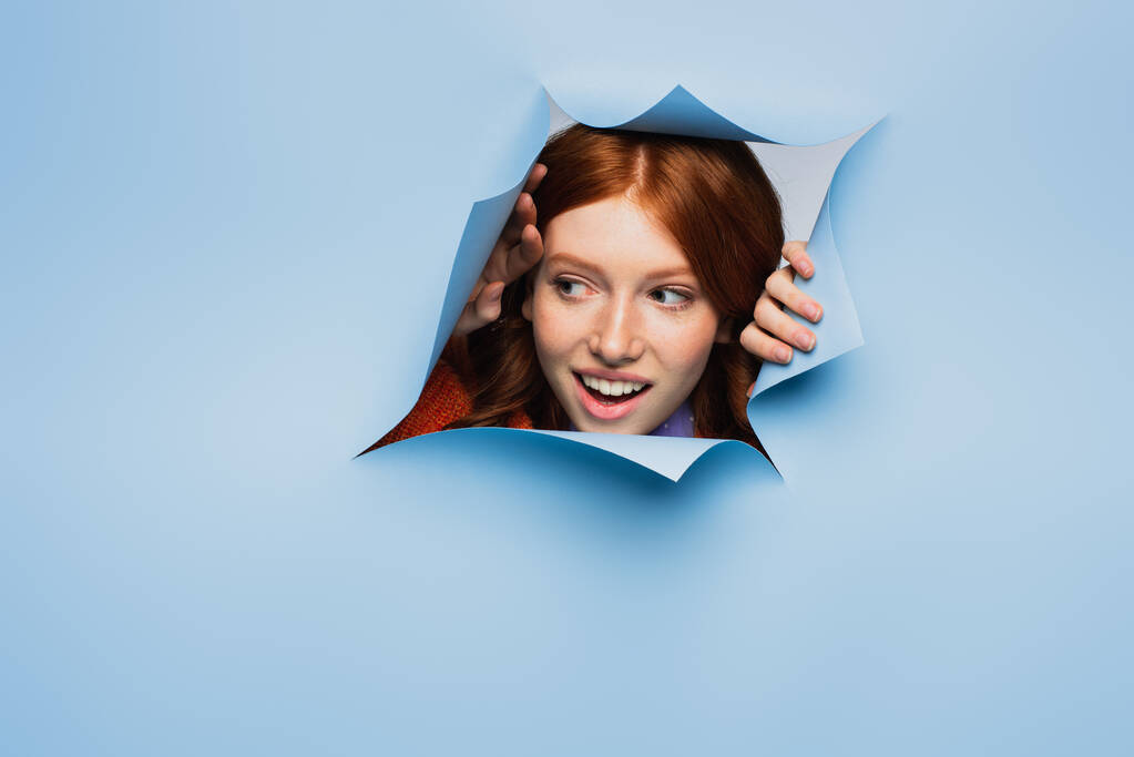 elképedt vörös hajú fiatal nő néz félre kék szakadt háttér - Fotó, kép