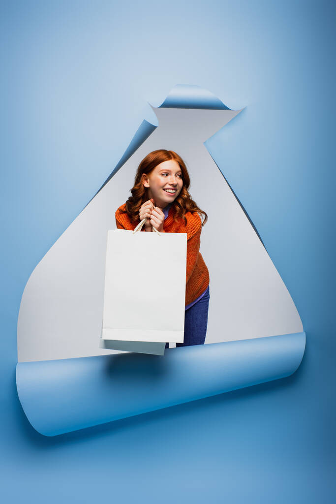 hymyilevä nuori nainen tilalla ostoskassi sininen revitty paperi tausta  - Valokuva, kuva