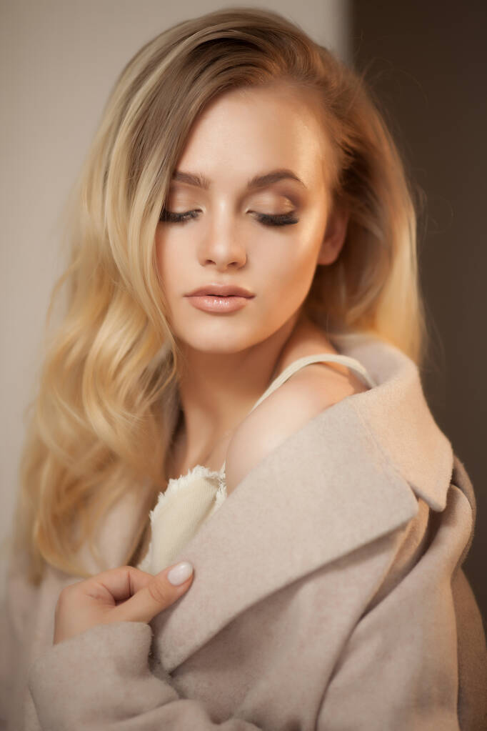 Portrait of a blonde woman wearing beige coat, looking over shoulder. Beautiful woman with everyday makeup. - Photo, Image
