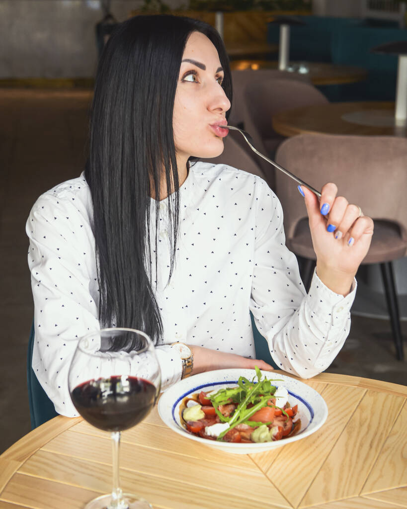 Jonge aantrekkelijke vrouw met een gezonde lunch in het restaurant. Blanke vrouw met zwart haar dineren. Uit eten concept, alleen eten in restaurant als gevolg van Covid-19 pandemie. - Foto, afbeelding