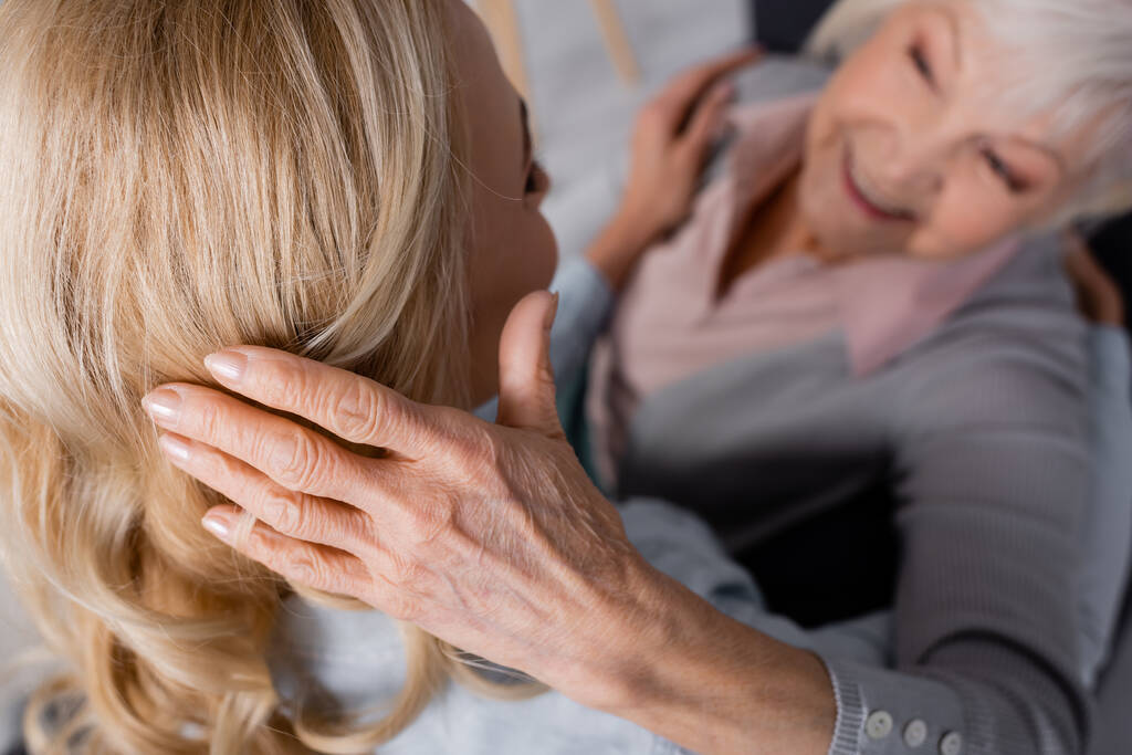 Geçmişi bulanık yaşlı bir kadın kızının saçına dokunuyor. - Fotoğraf, Görsel