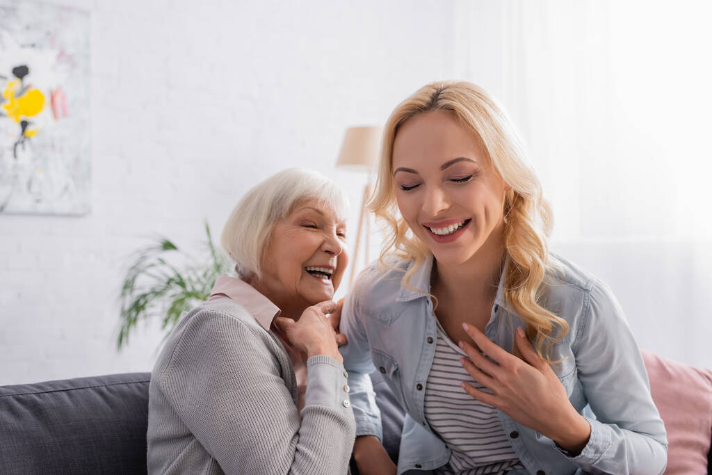 Mujer alegre sentada cerca de la madre anciana en el sofá  - Foto, imagen