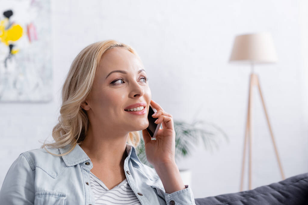 Femme blonde souriante parlant sur smartphone à la maison - Photo, image