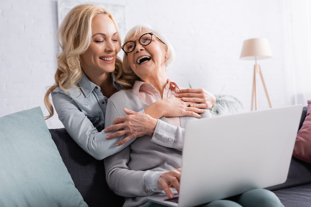 Veselá žena objímající starší matku s rozmazaným notebookem doma  - Fotografie, Obrázek